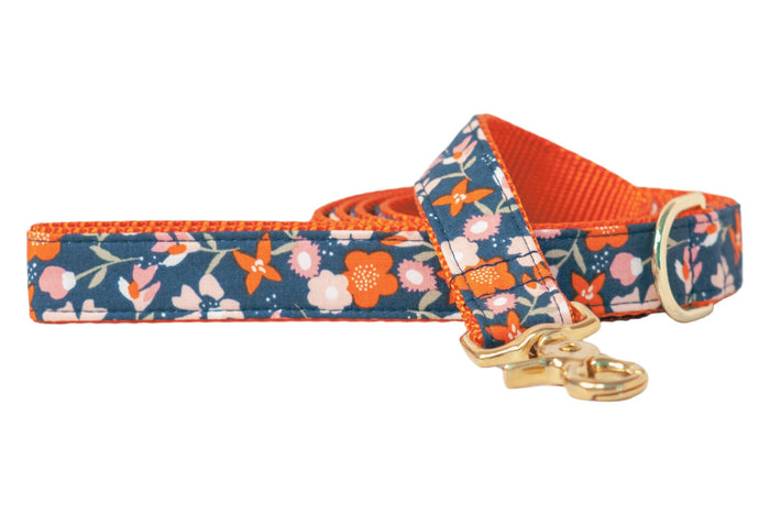 Dog leash with a dark navy blue fabric with a fall floral pattern featuring small blossoms and leafy stems. The fabric is stitched over sturdy nylon webbing and the leash is finished with a polished swivel clasp and a matching D-ring near the handle.