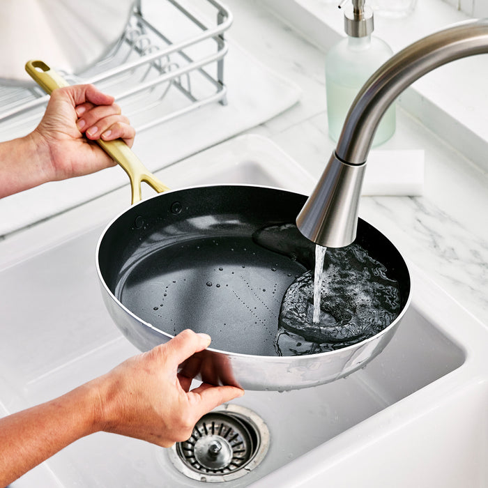 GP5 stainless steel frying pan with champagne handle being rinsed under water in a kitchen sink.