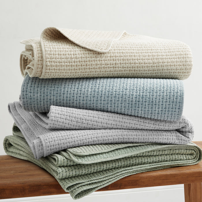Pick-Stitch Artisan Quilted Throw in various colors stacked on a wooden surface, showcasing its textured and cozy design.