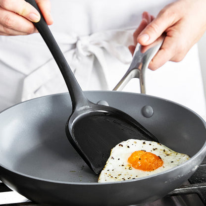 Person wearing a white apron lifts a fried egg with a black silicone spatula from a 5-piece utensil set.