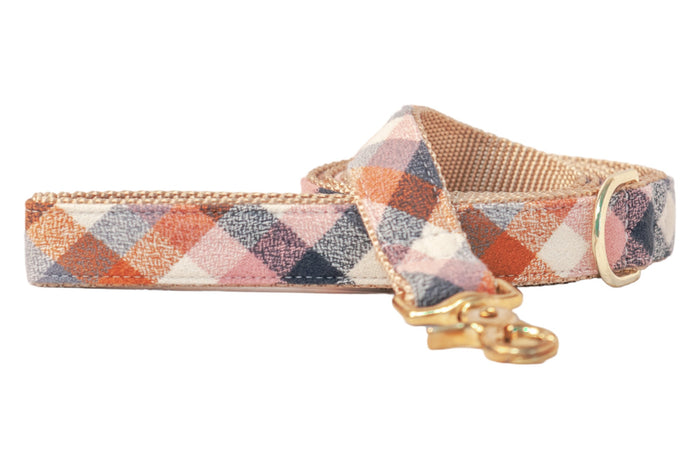 Dog leash made of flannel fabric with a small checkered plaid pattern in warm fall colors. The leash features a tan woven backing, metal hardware, a D-ring, and a swivel clasp for secure attachment.