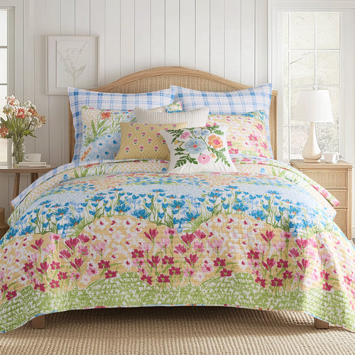 Floral bedding set on a bed in a bedroom with a lamp and flowers.