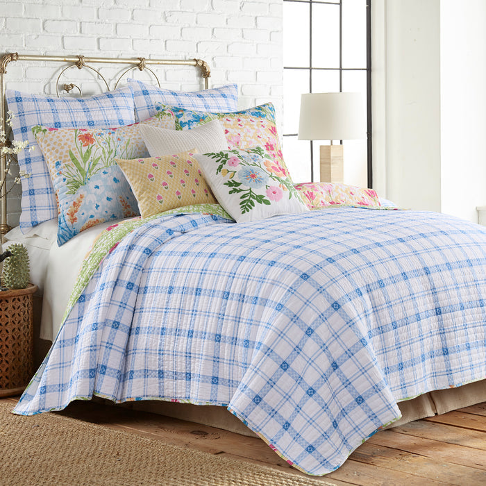 Bed with floral pillows and a blue plaid comforter in a bright bedroom.