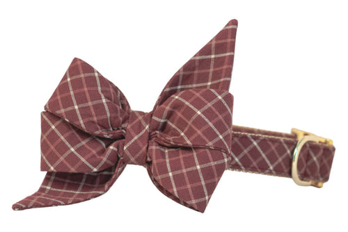 Burgundy dog collar adorned with a dramatic belle bow that features exaggerated, feminine pointed ends. The entire piece is patterned in an autumnal plaid pattern, with metal hardware providing a sleek contrast.