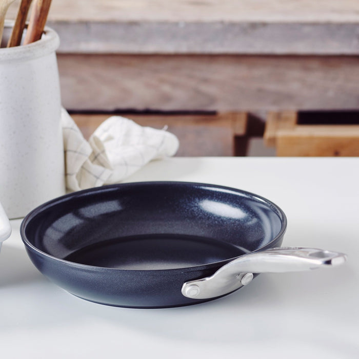 Black ceramic 8-inch frypan with metal handle on a white countertop next to a folded towel.