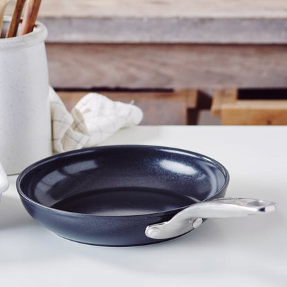 Black ceramic 8-inch frypan with metal handle on a white countertop next to a folded towel.