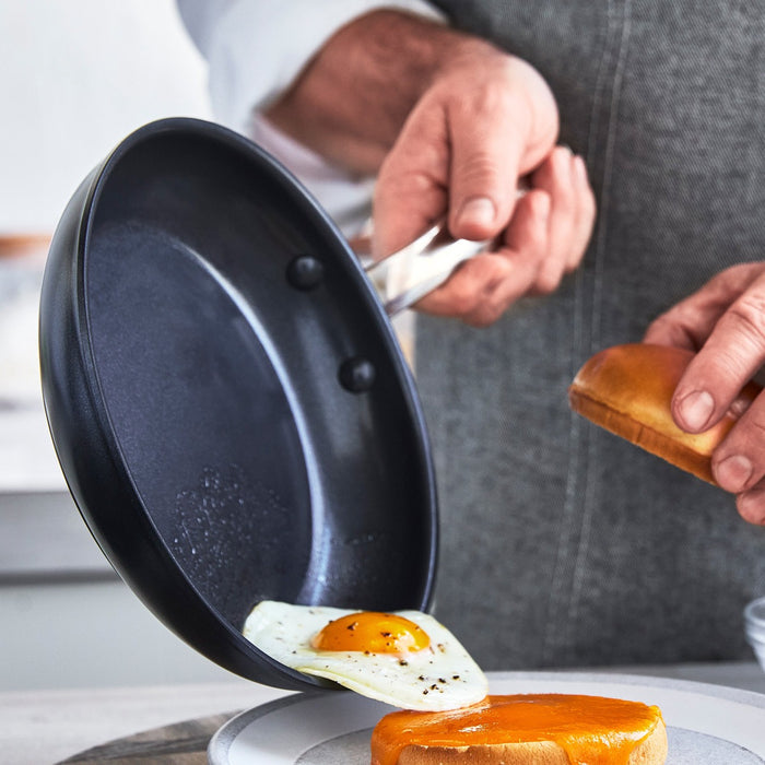 Fried egg being slid from a black ceramic 8-inch frypan onto a plate with a bun.