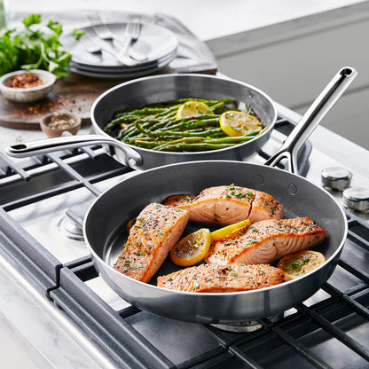 Two GP5 stainless steel frypans on stove, one with salmon and lemon, the other with asparagus and lemon.