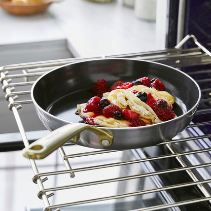 Stainless steel frypan set with champagne handles holding pancakes and mixed berries on an oven rack.