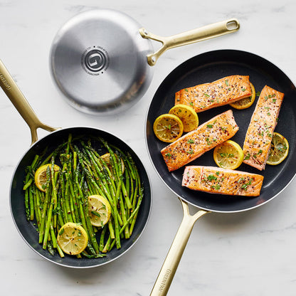 Stainless steel frypan set with asparagus and lemon in one pan, salmon fillets with lemon in the other.