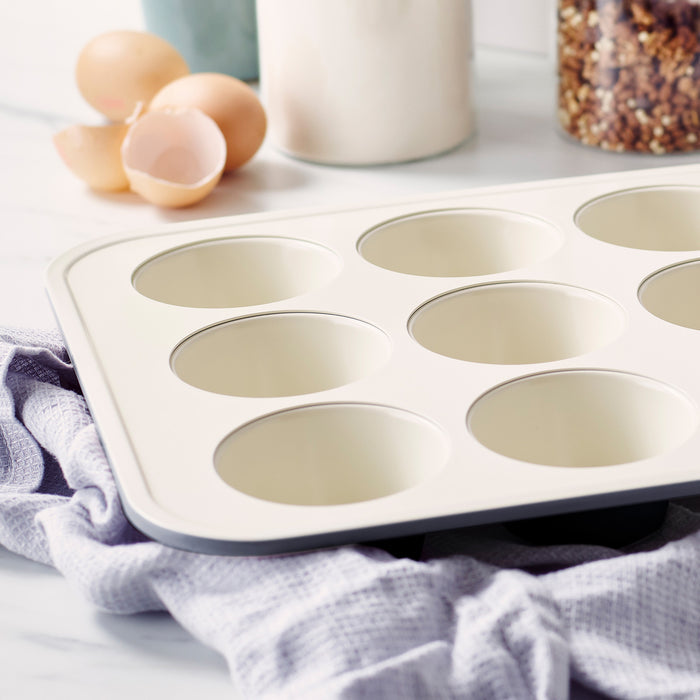 Black ceramic muffin pan on a kitchen towel with eggshells and baking ingredients in the background.