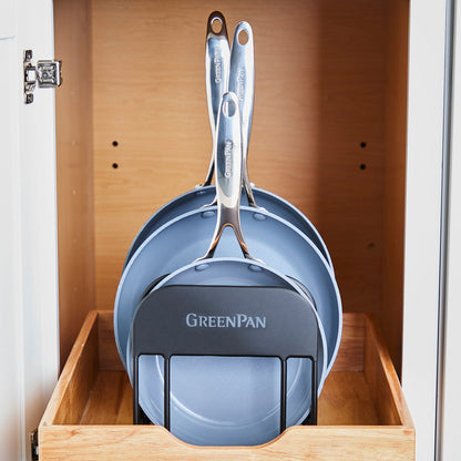 Set of three blue frying pans with metal handles, stored upright in a wooden drawer on a cookware rack.