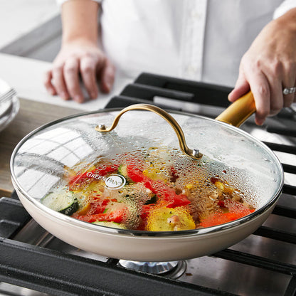 GreenPan Reserve 10 skillet with matte gold handle on stove, glass lid covering sautéed vegetables.
