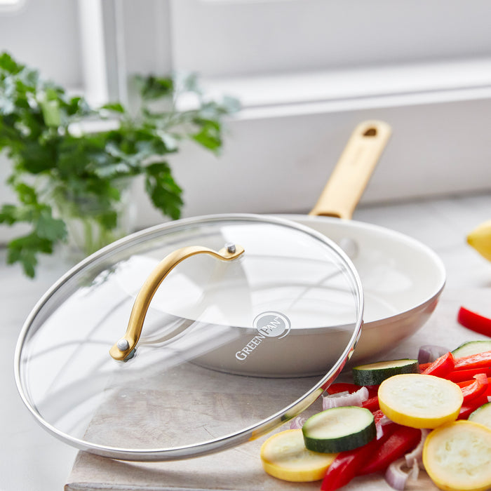 Clear glass lid with green handle, 8-inch size, resting beside sliced vegetables on a bright kitchen counter.