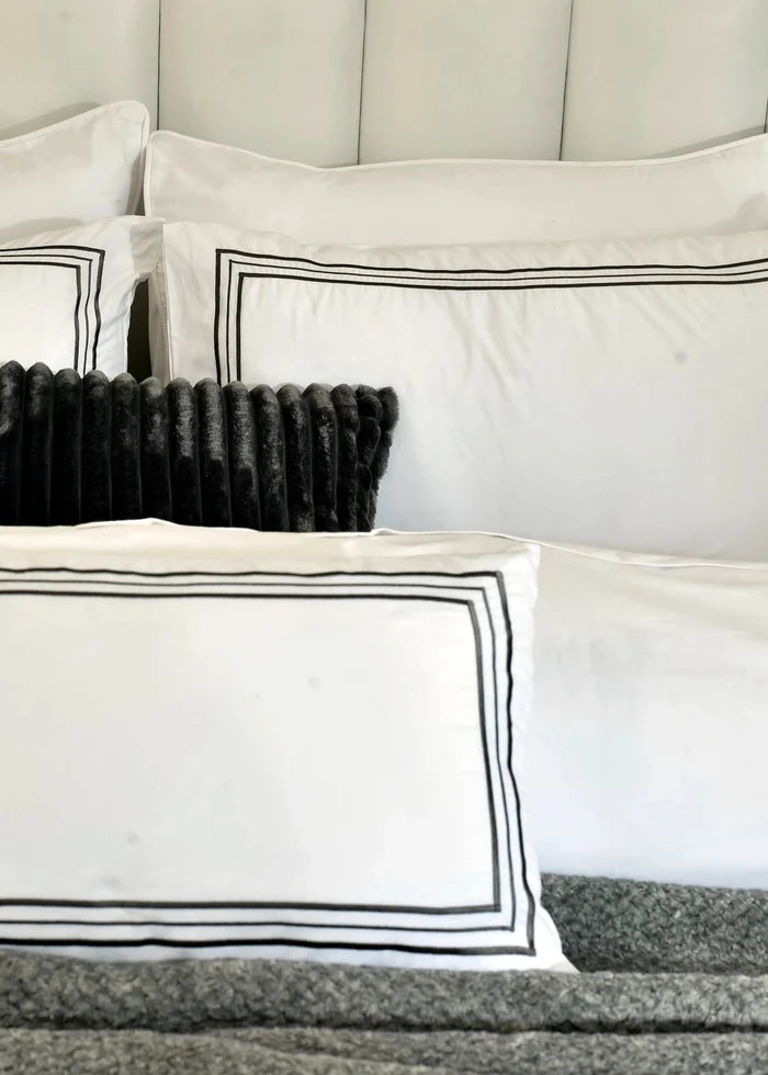 White pillow shams with black border stripes and dark tufted cushion