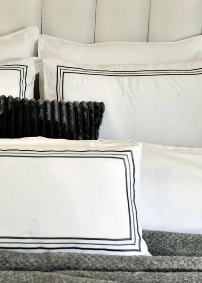 White pillow shams with black border stripes and dark tufted cushion