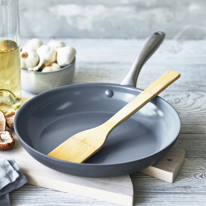 Ceramic 10-inch frypan with bamboo spatula, garlic cloves, and oil on a light wood surface.