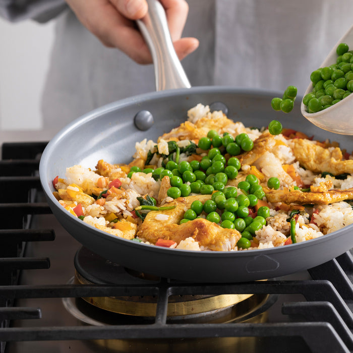 Gray ceramic 10 frypan with bamboo spatula on stove, cooking fried rice and green peas.