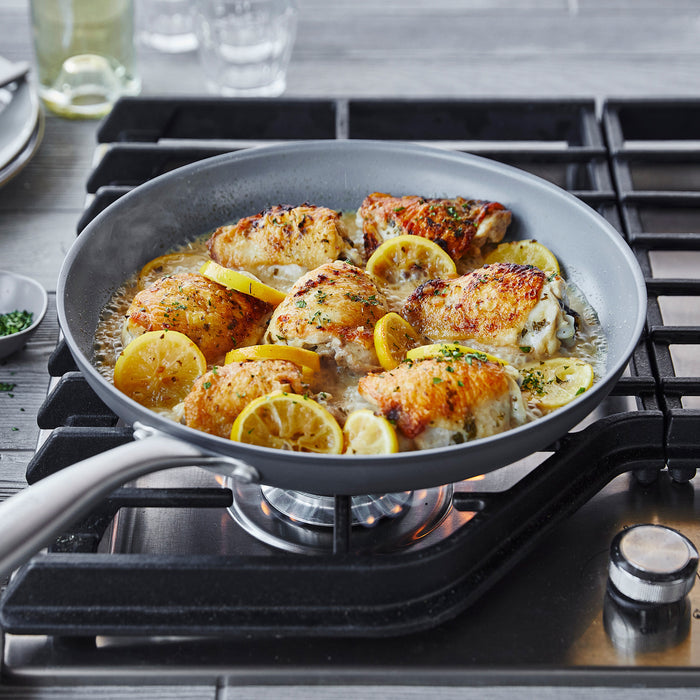 Chicken thighs with lemon and herbs cooking in a green ceramic nonstick frypan, stirred with a bamboo spatula.