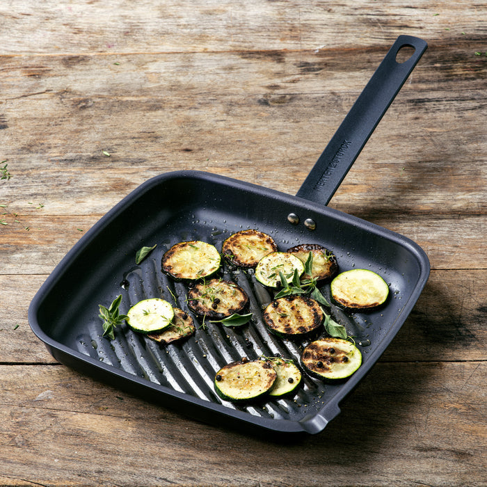 Grilled zucchini in a carbon steel 11-inch square grill pan on a rustic wooden table.