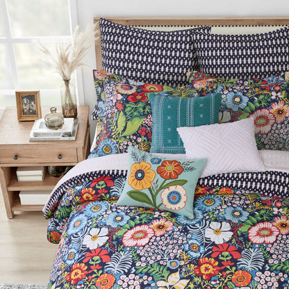 Colorful floral bedding set on a bed with a wooden nightstand in the background.