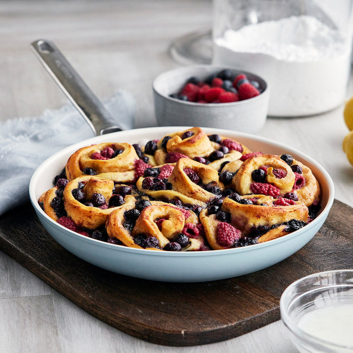 Baked berry sweet rolls next to two Padova Pro ceramic nonstick frypans and baking ingredients on a kitchen counter.