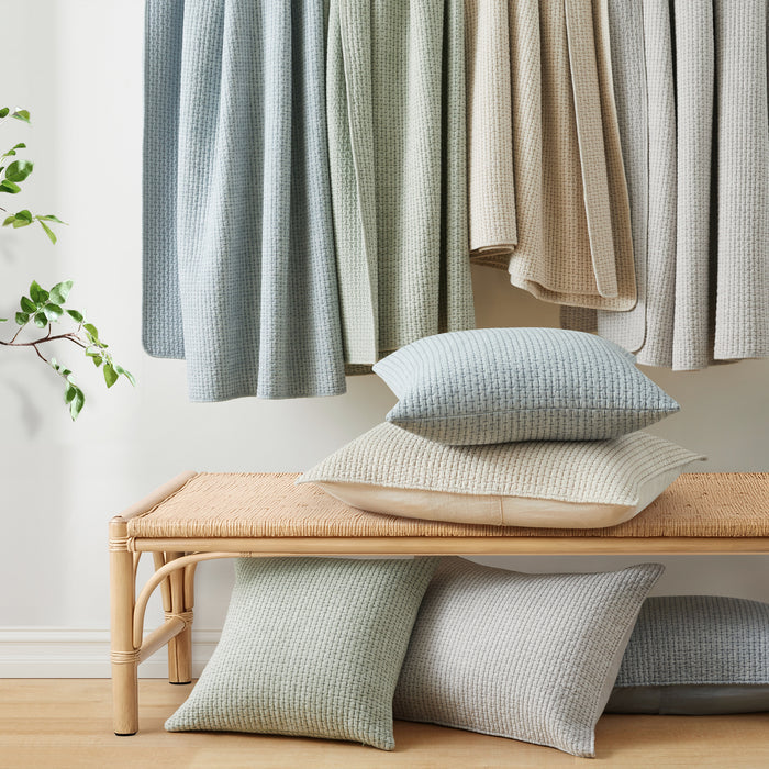 Textured cushions on a wooden bench with light-colored curtains in the background