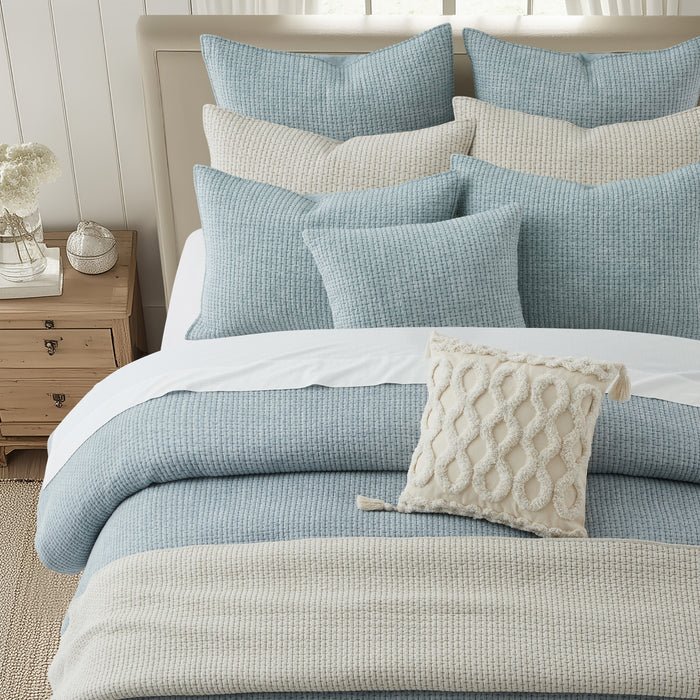 Pick-Stitch Artisan Square Pillow on a cozy layered bed with blue and cream pillows.