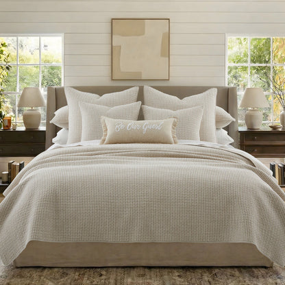 Neatly made bed with beige bedding and pillows in a well-lit bedroom.