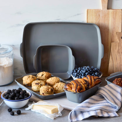 Gray ceramic nonstick square baker filled with scones, rolls, and berries sitting on a kitchen counter.