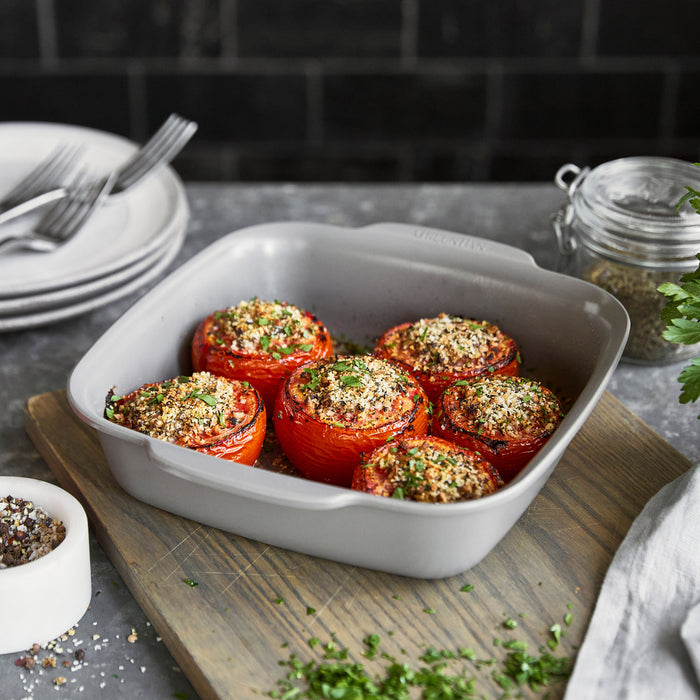 Stuffed tomatoes in an 8x8 white ceramic square baker on a countertop.