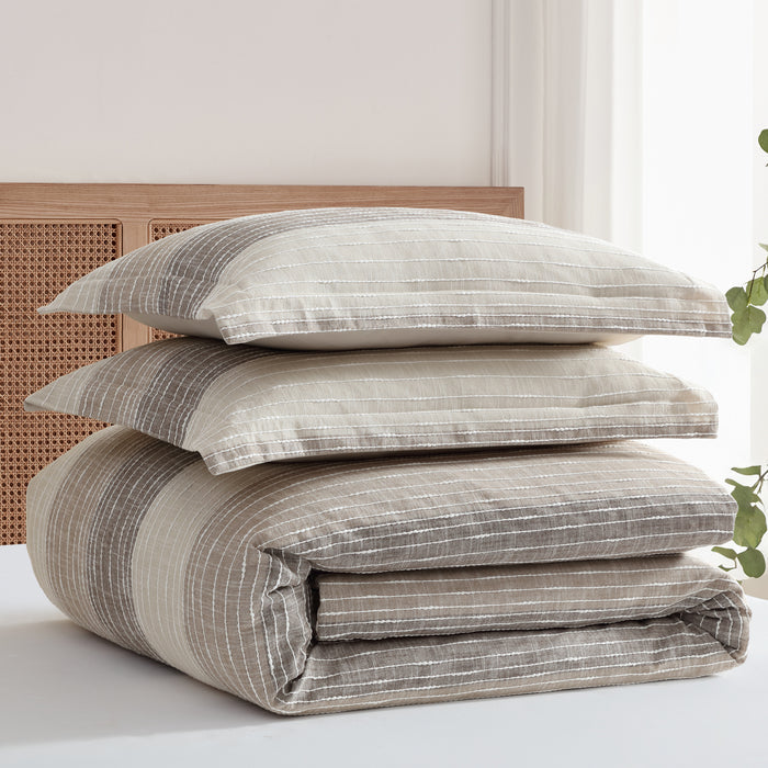 Stack of striped bedding and pillows on a bed with a light background