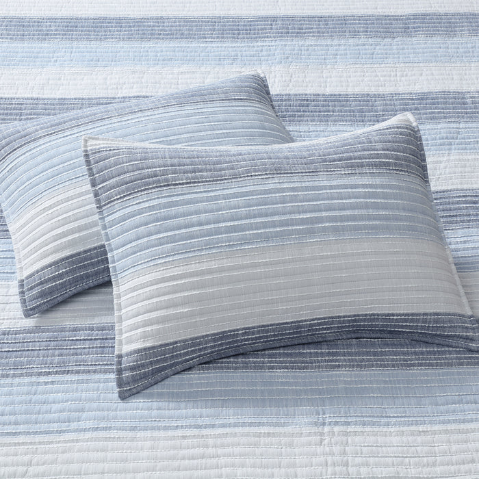 Sand Stripes Blue Quilt with two textured pillows in shades of blue and white, showcasing coastal-inspired design.