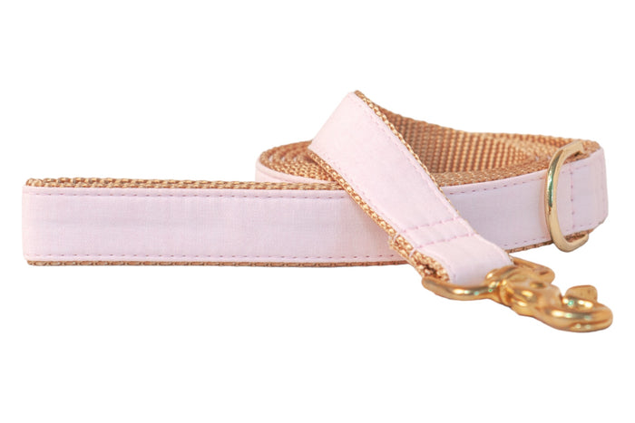 A handcrafted dog leash made from solid pale pink linen fabric layered over durable nylon webbing. The leash features reinforced stitching along the edges, a coordinating pink handle for comfort, and a polished metal swivel snap hook for secure collar or harness attachment. A matching gold D-ring sits near the handle for convenient accessory clipping.