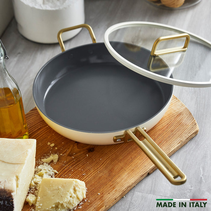White ceramic nonstick 12-inch frypan with lid on wood surface, next to olive oil and cheese.
