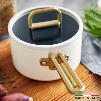 White ceramic saucepan with lid on wood, surrounded by fresh herbs, onions, and spices. 2-quart size.