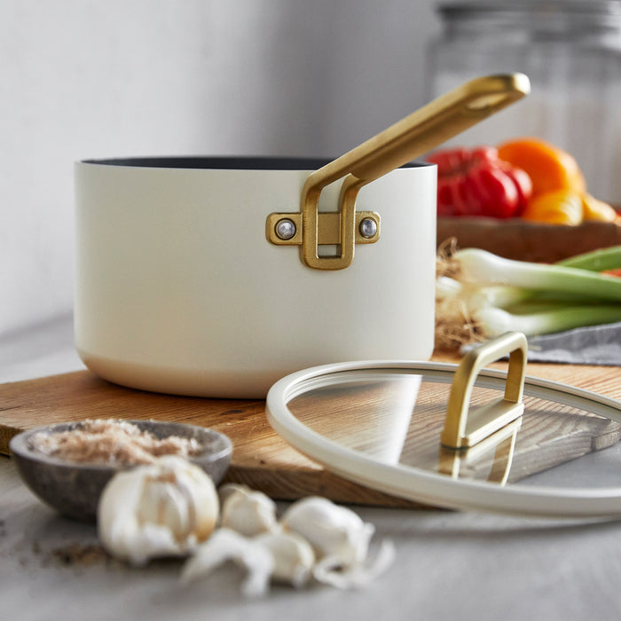 White ceramic nonstick saucepan with a gold handle on a wooden board.