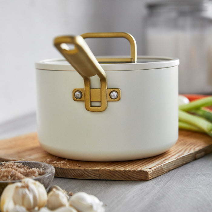 White ceramic nonstick 4-quart saucepan on a wooden cutting board next to garlic and assorted vegetables.