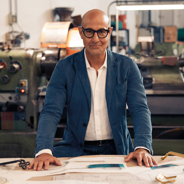 Stanley Tucci 4-quart stainless steel saucepan on worktable with blueprints; man in glasses and blue blazer stands behind.