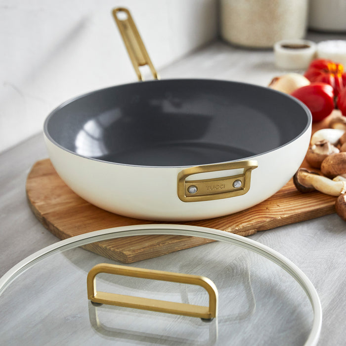 White ceramic 6.5-quart pan with gold handle on a board, matching lid placed in front.