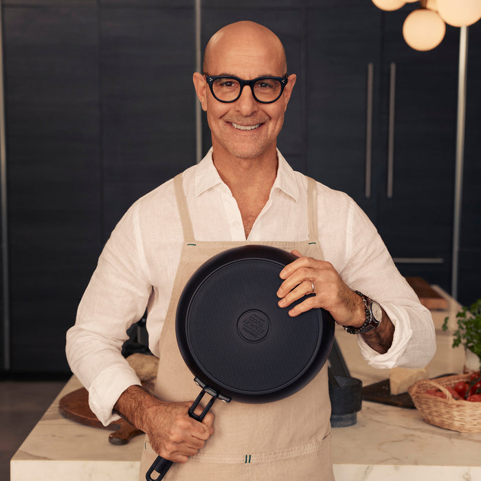 Man in glasses and apron holding a black Stanley Tucci 6.5-quart pan.