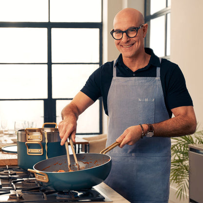 Man in glasses and apron cooking with a Stanley Tucci ceramic nonstick pan in a modern kitchen.