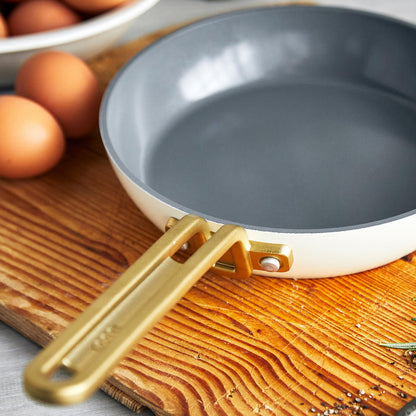 White ceramic nonstick frypan set on a board beside brown eggs.