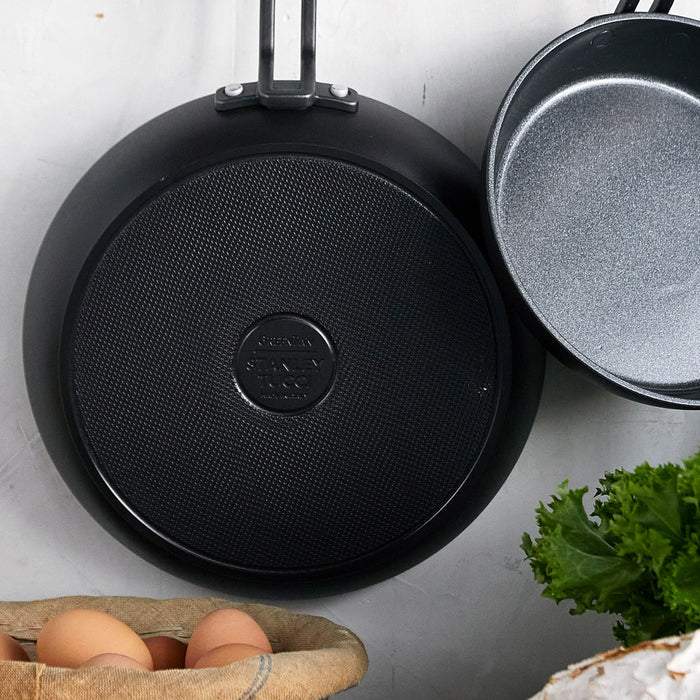 Two ceramic nonstick frypans, 8 and 10, with eggs and leafy greens on a light surface, top view.