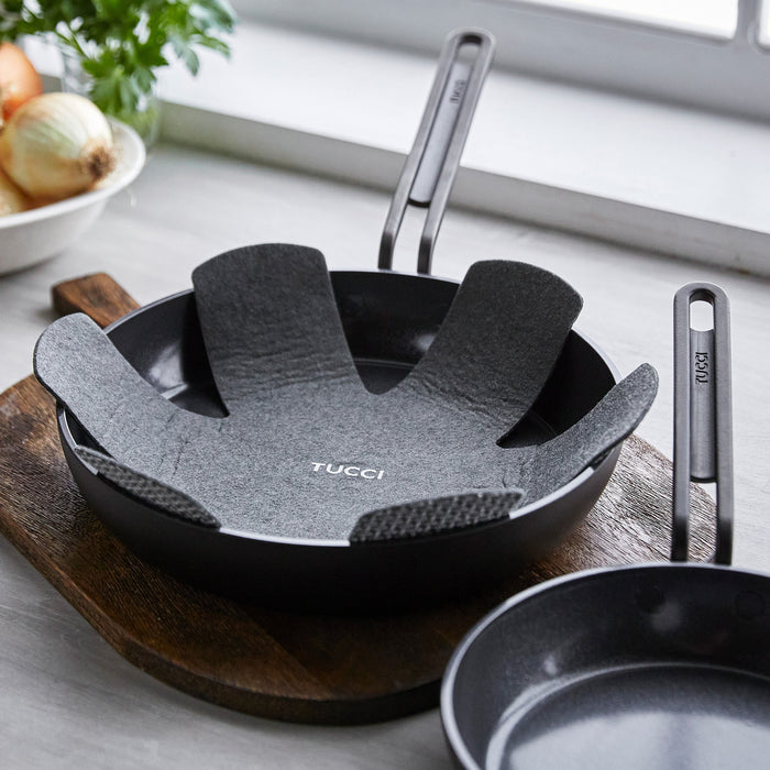 Set of two black ceramic nonstick frypans with liners on a board next to whole onions.