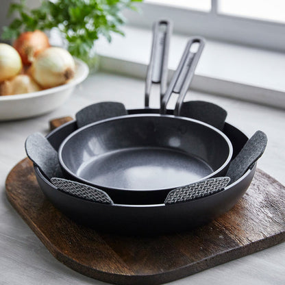 Two ceramic nonstick frypans with pan protectors, stacked near a bowl of onions on a windowsill.