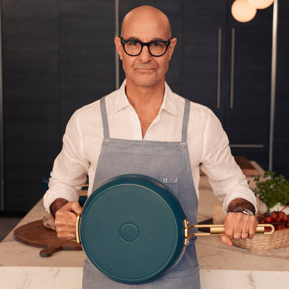 Stanley Tucci holding a teal saute pan in a kitchen