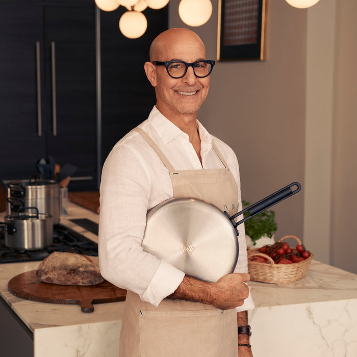 Man in glasses and apron holding a 12-inch stainless steel nonstick frypan with a black handle.