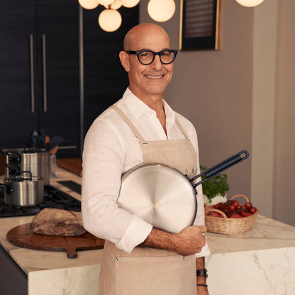 Man in glasses and apron holding a 12-inch stainless steel nonstick frypan with a black handle.
