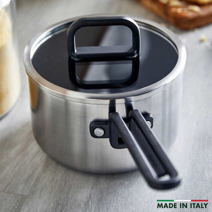 Stainless steel 2-quart saucepan with black handle and glass lid on a gray countertop.